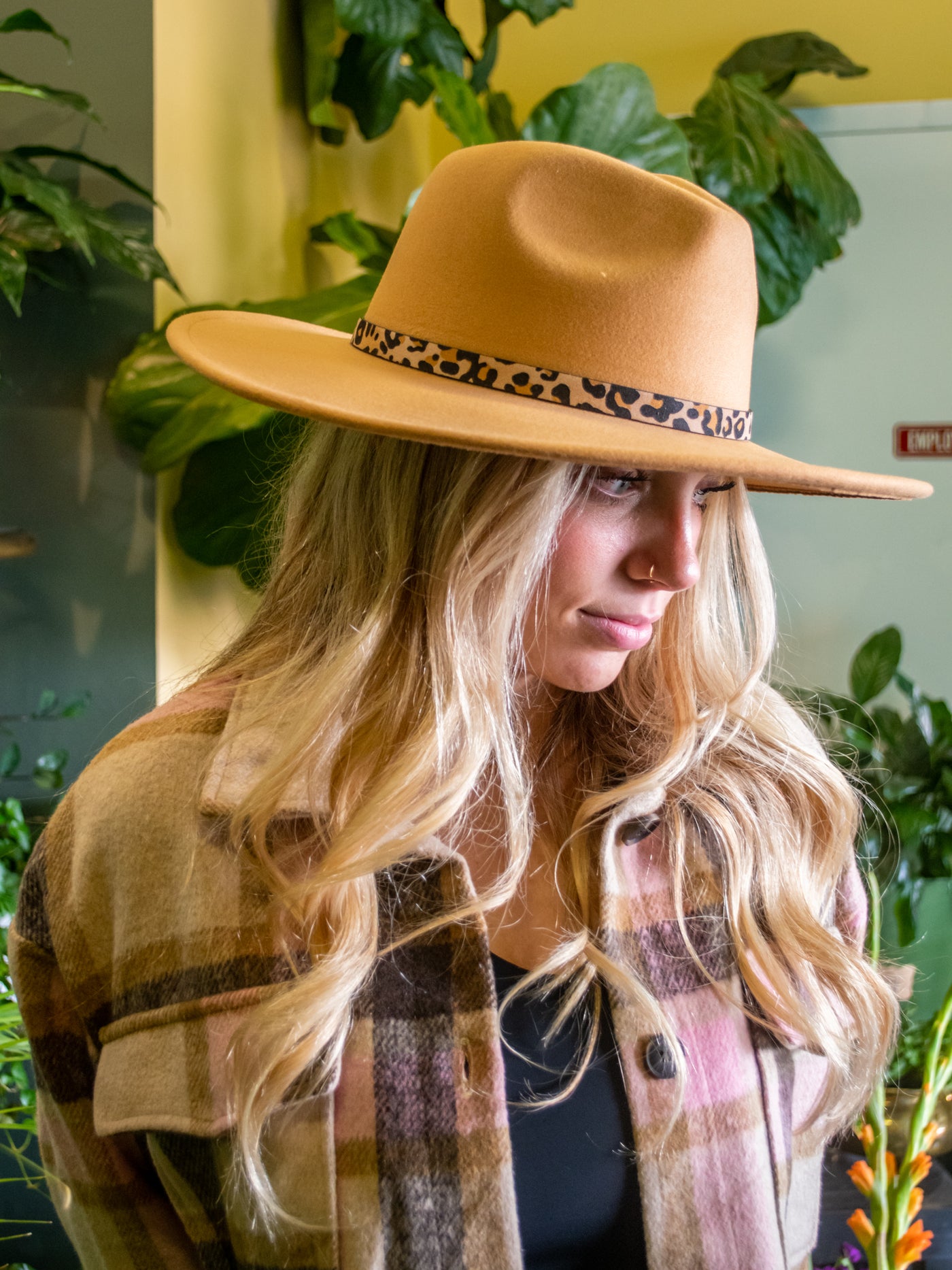 A model wearing a tan wide brim hat with a leopard band around it. She has it on with a plaid shacket and pleather pants.