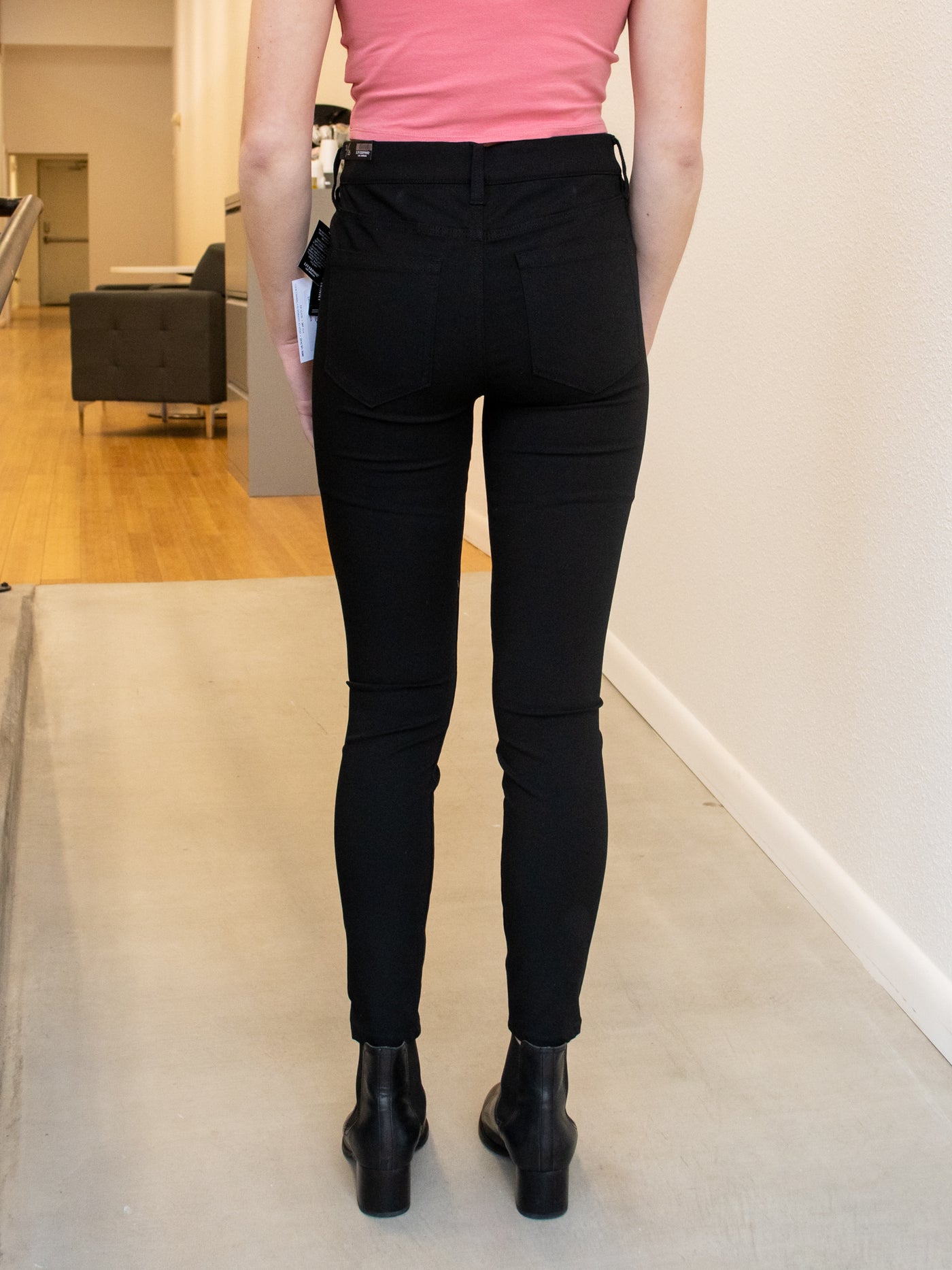 A model wearing a pair of black ankle length skinny pants with a pink tank, plaid blazer, and black booties.