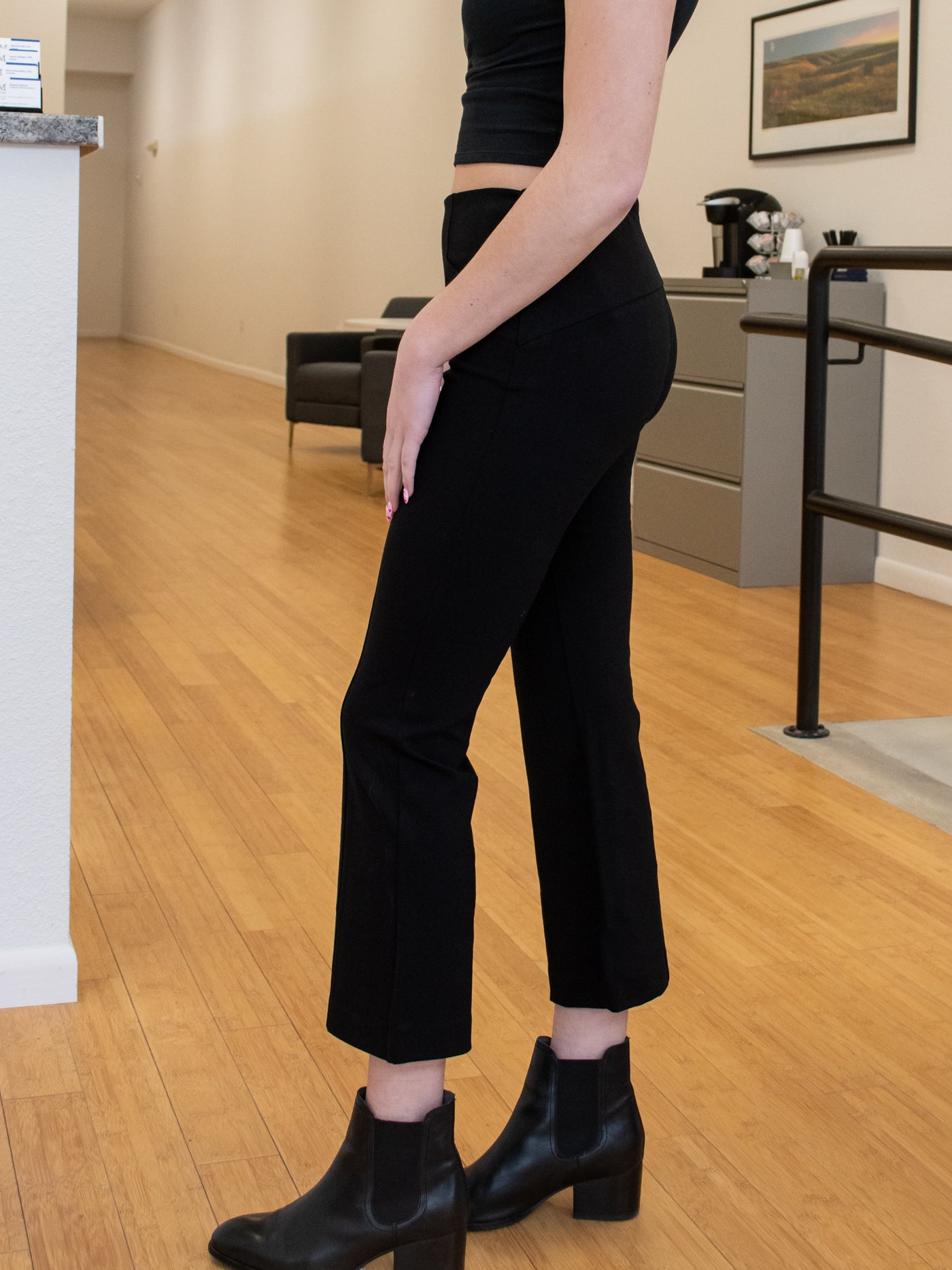 A model wearing a pair of black kick flare pants with welt pockets. She has it on with black boots and black top.