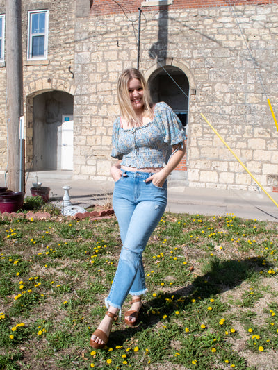 A model wearing a pair of non-skinny skinny jeans with a fray hem and subtle destruction. She has them on with a floral top and brown platform sandals.