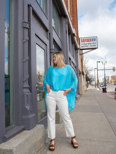 A model wearing a pair of white cropped straight leg jeans with a cut hem. She has them on with a turquoise blouse and brown platform sandals.