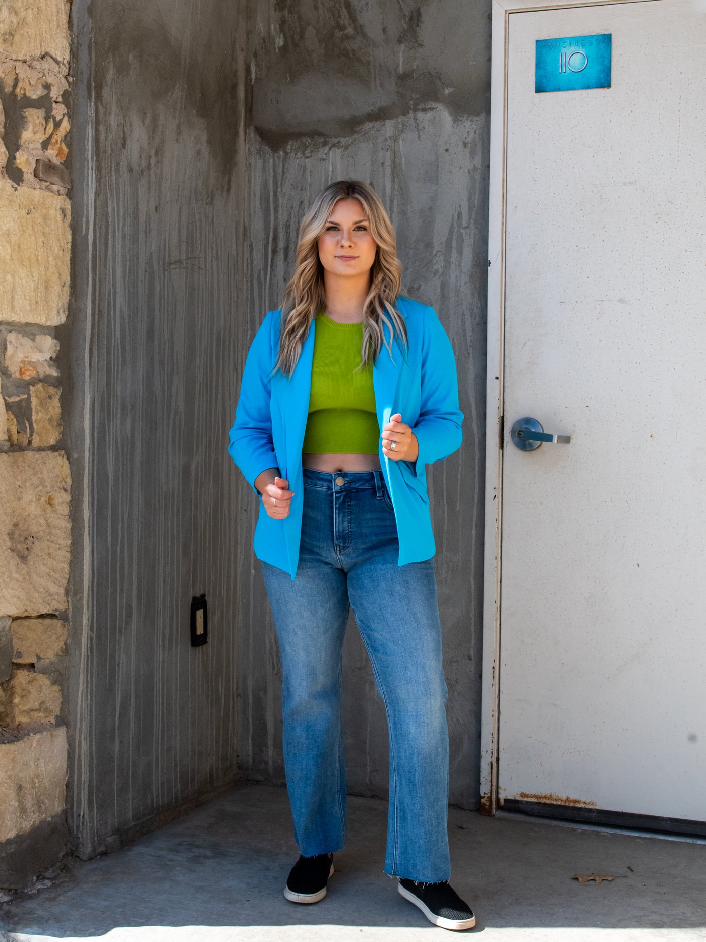 A model wearing a bright blue shirred sleeve blazer over a green tank with denim.