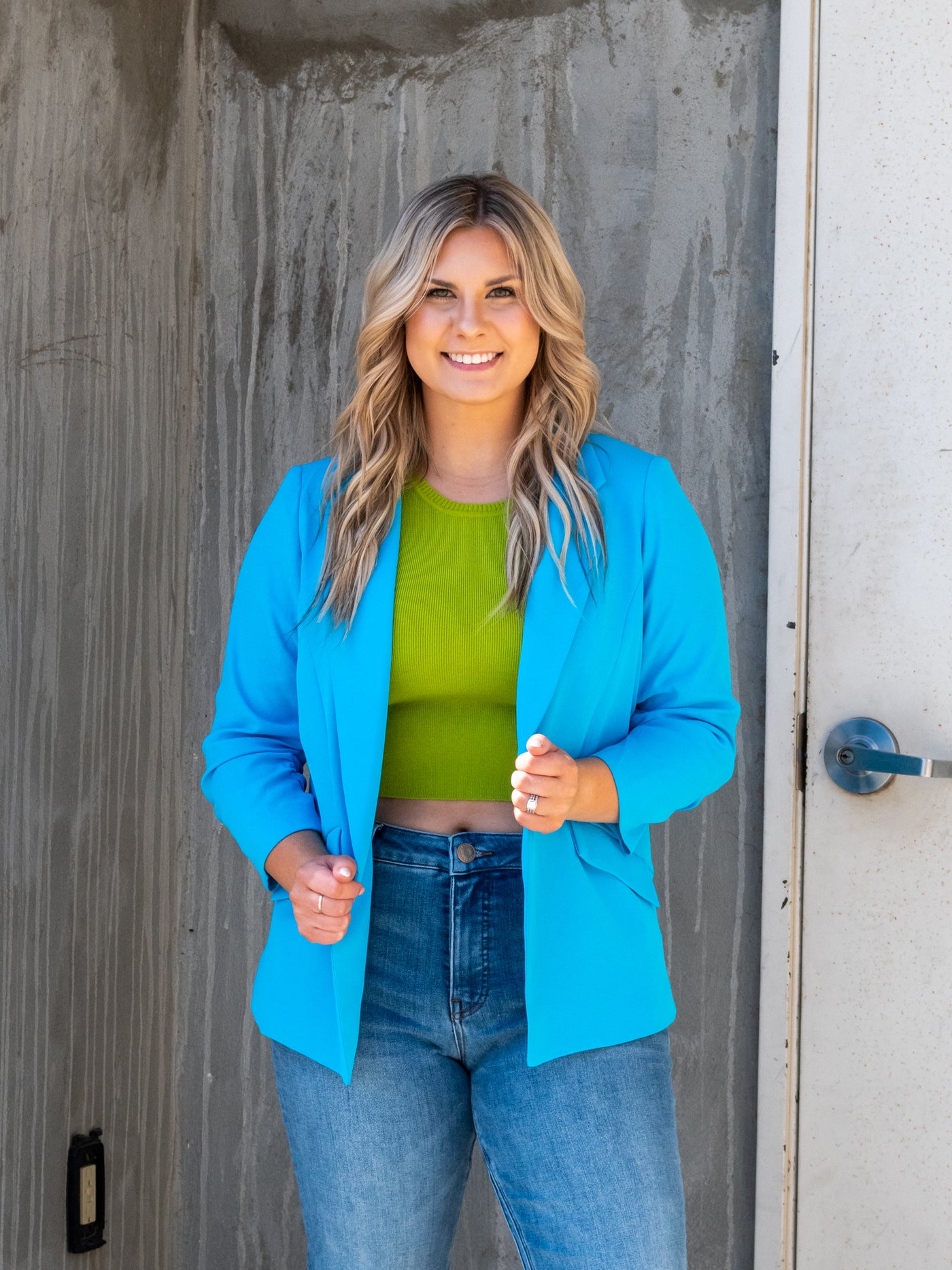 A model wearing a bright blue shirred sleeve blazer over a green tank with denim.