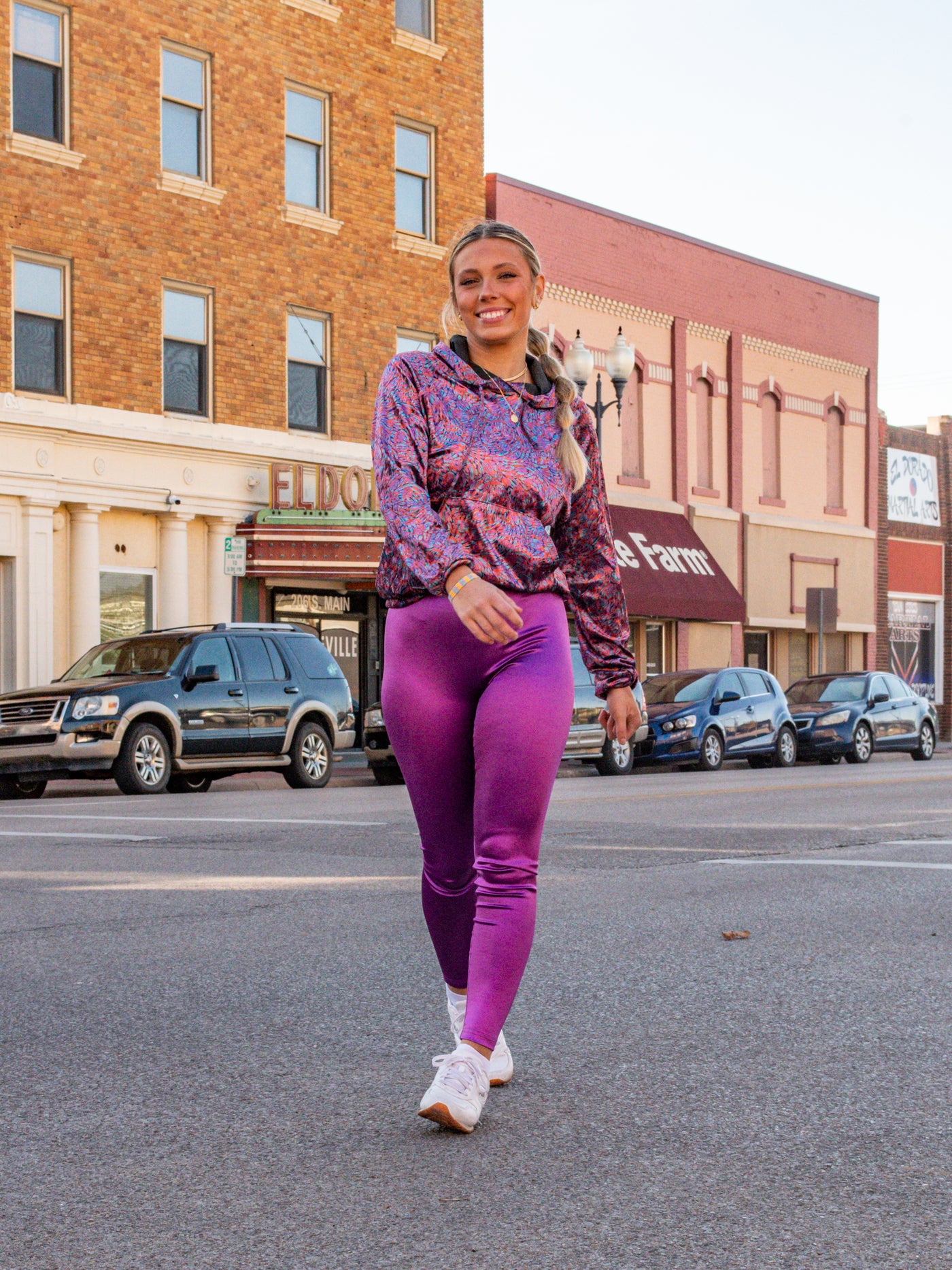 A model wearing a pair of bright purple iridescent leggings and a multicolor printed hoodie.