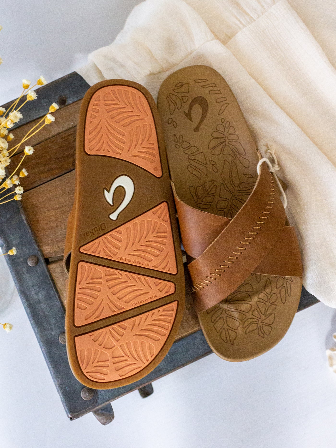A brown leather slide style sandal that has two crossover straps and stitching detail on the top one.