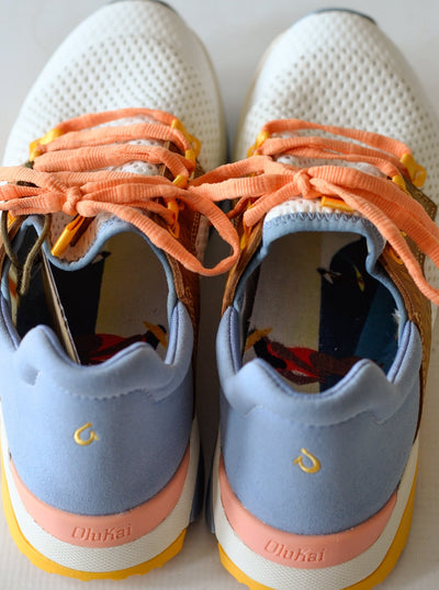 A white fashion sneaker with peachy orange laces, brown leather details, a light blue suede back, and colorful rubber bottoms.
