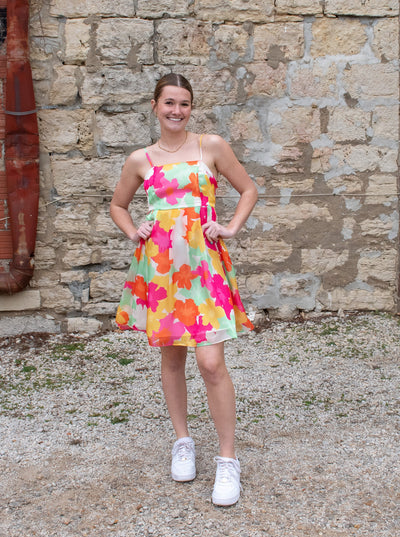 A model wearing a bright floral print chiffon mini dress with spaghetti straps.