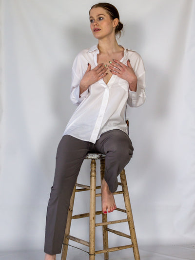 A model wearing a pair of dark grey colored cigarette pants and a white button down blouse.