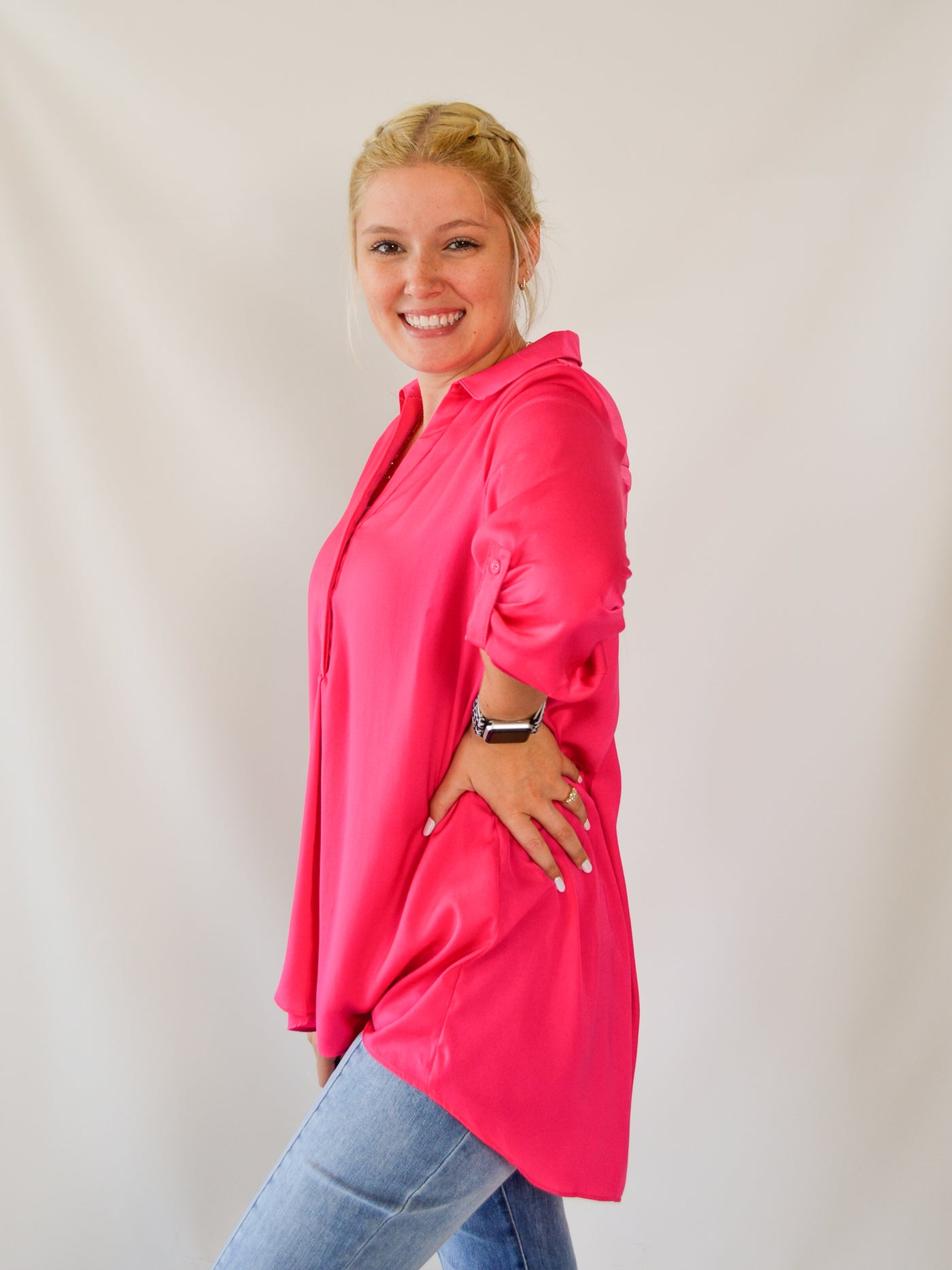 A model wearing a hot pink colored airflow blouse. The blouse is longer in the back than the front. She has it paired with denim jeans.