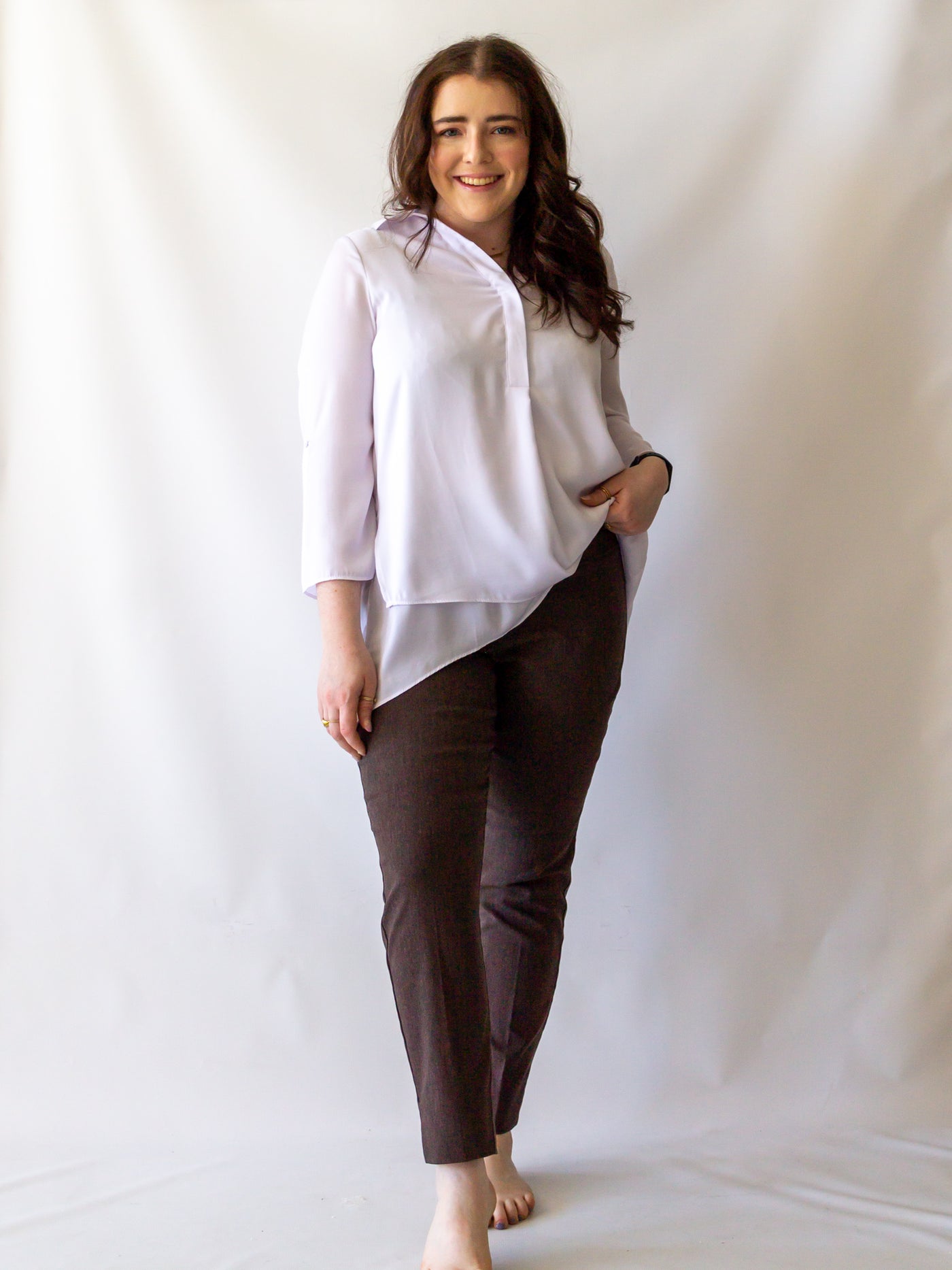 A model wearing a pair of heather brown colored cigarette pants and a white blouse.