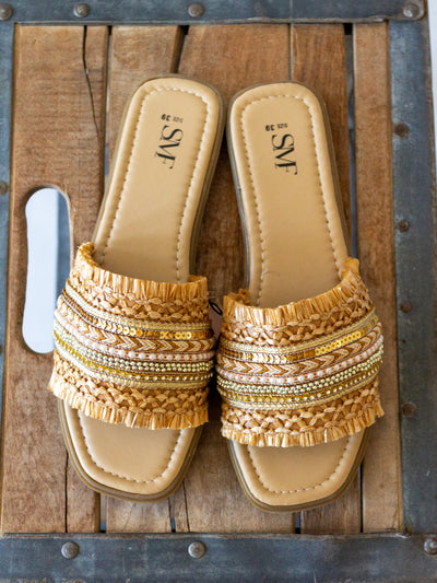 A boho themed sandal with braided, beads, sequins and other little accents on the top strap of the slide. They are shades of gold, brown, tan; neutral colors.