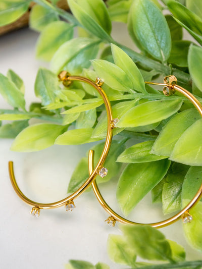 A pair of gold plated hoop earrings with CZ stones around them.