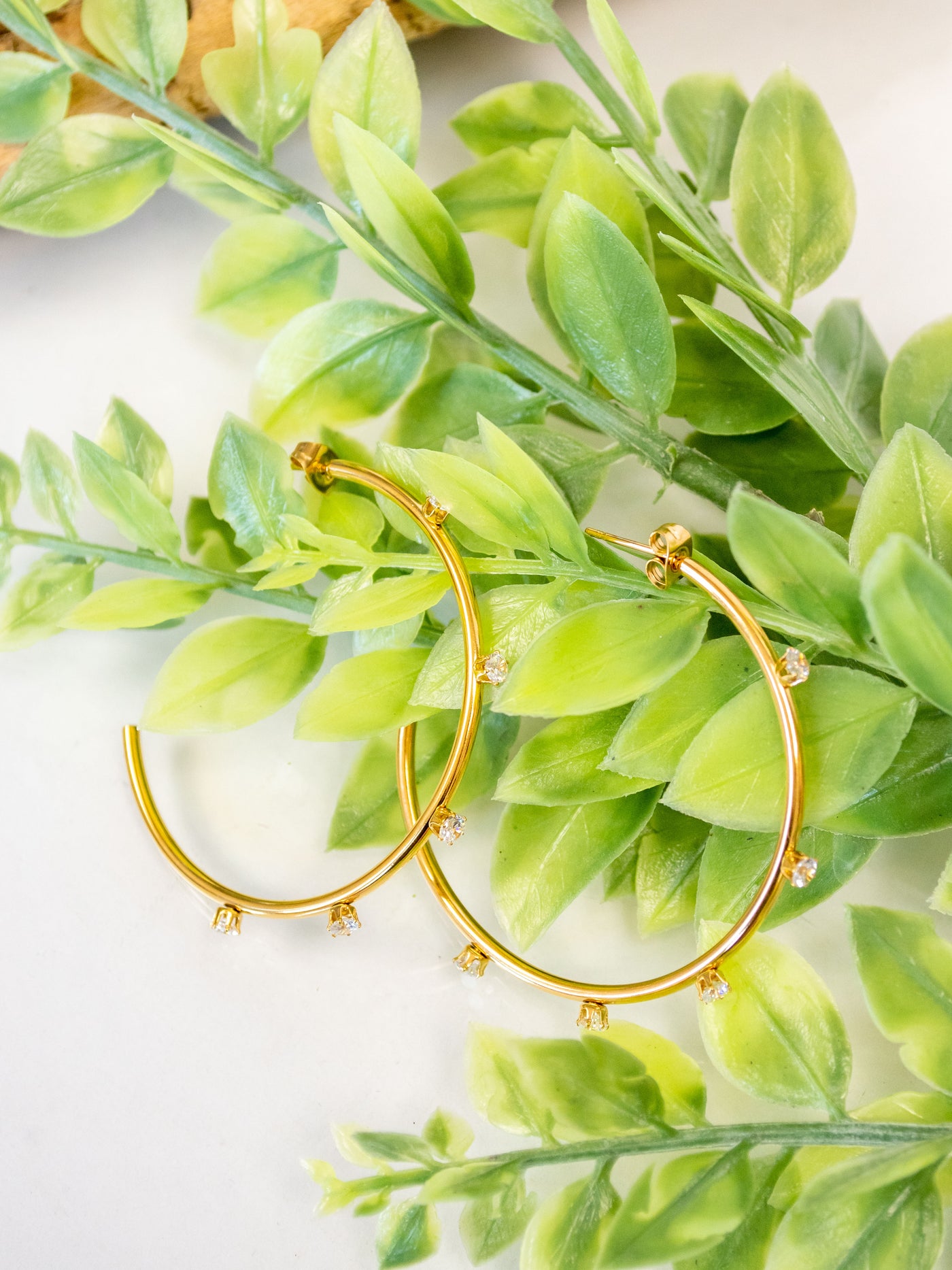 A pair of gold plated hoop earrings with CZ stones around them.