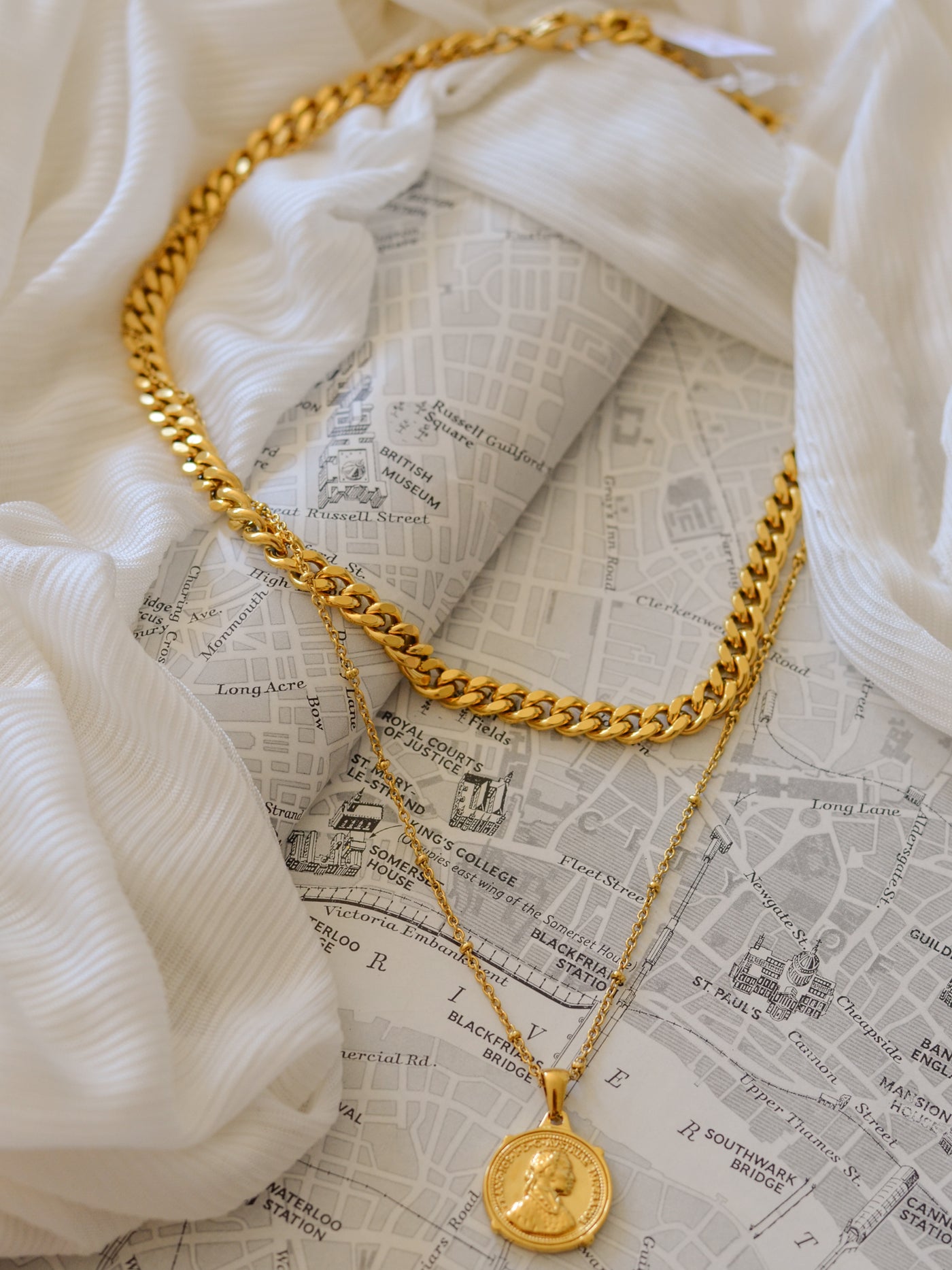 A double layer necklace with a long chain and ball chain with a coin and a shorter cuban chain necklace.