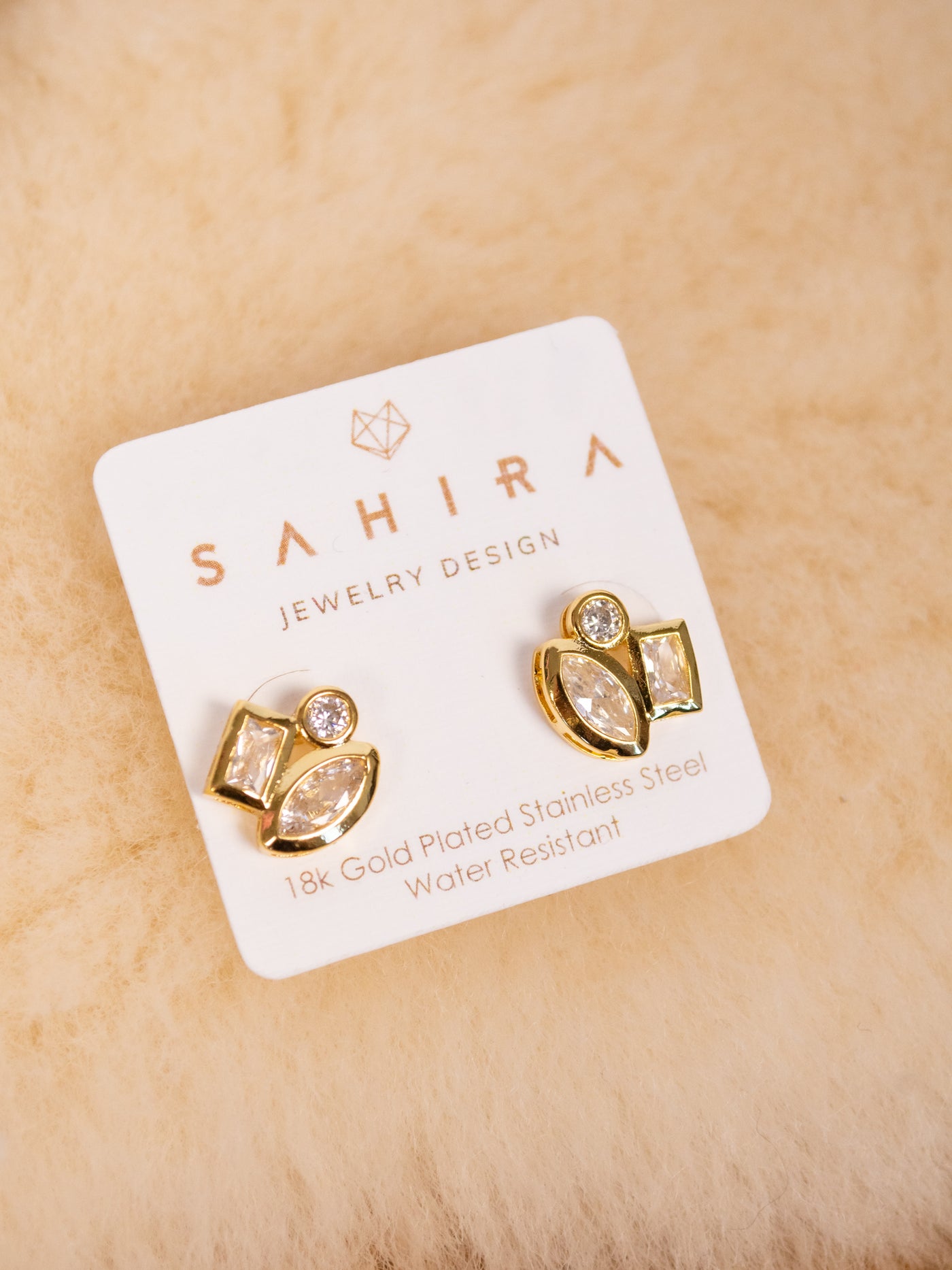 A pair of gold studs with three CZ stones on the from. One is circular, one oval, and one rectangle.