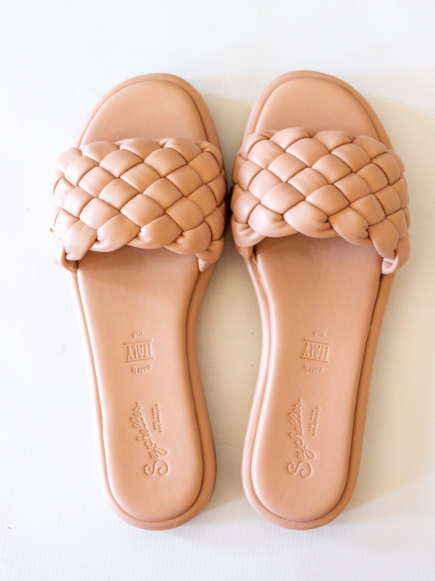 A pair a blush pink braided slide sandals.