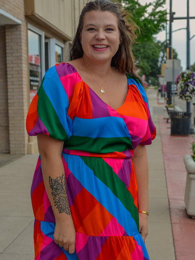 A model wearing a maxi dress with a v neck, puff sleeves, and a colorblock pattern.