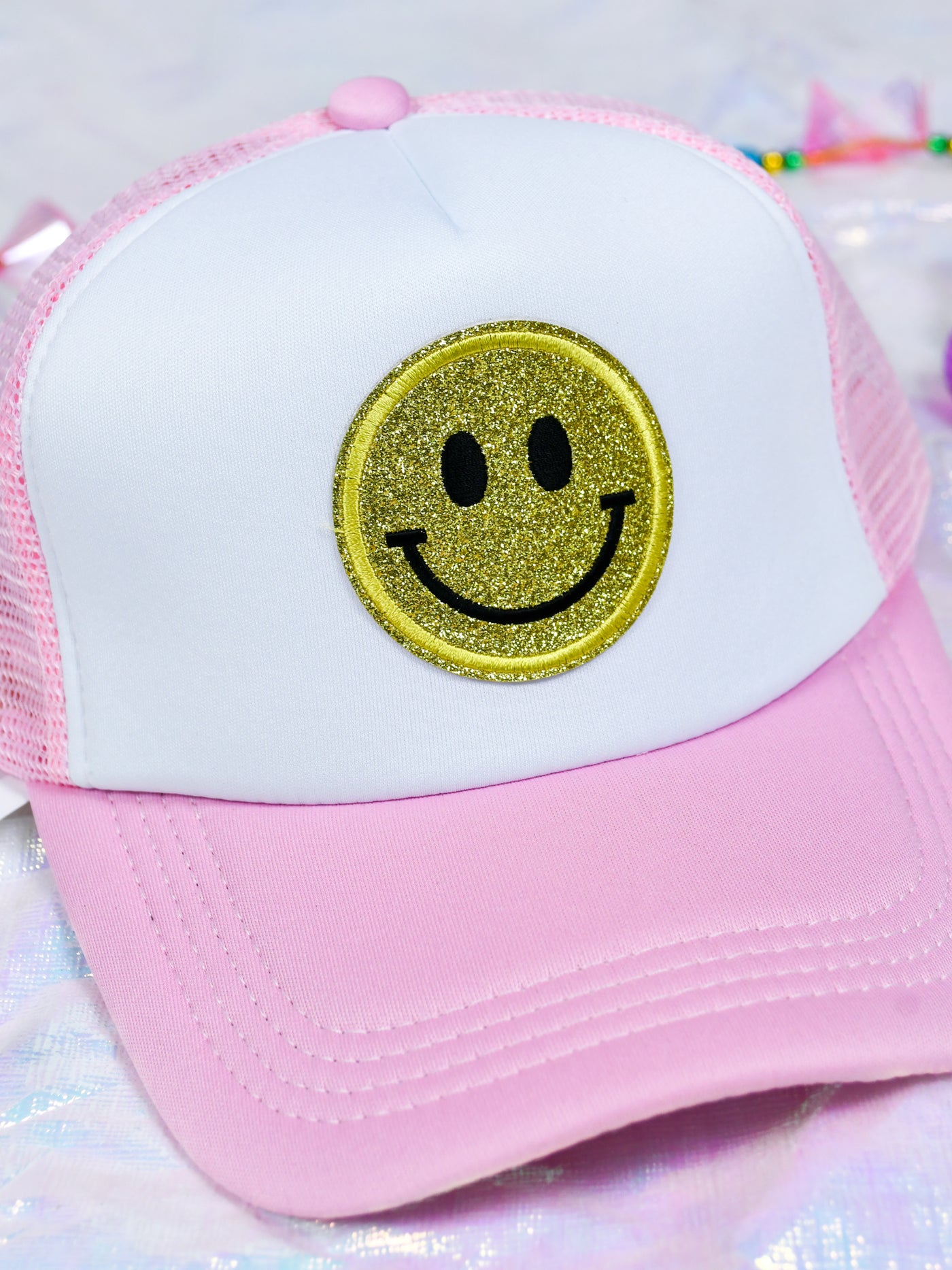 A model wearing a pink trucker hat with a yellow smiley face on the front.