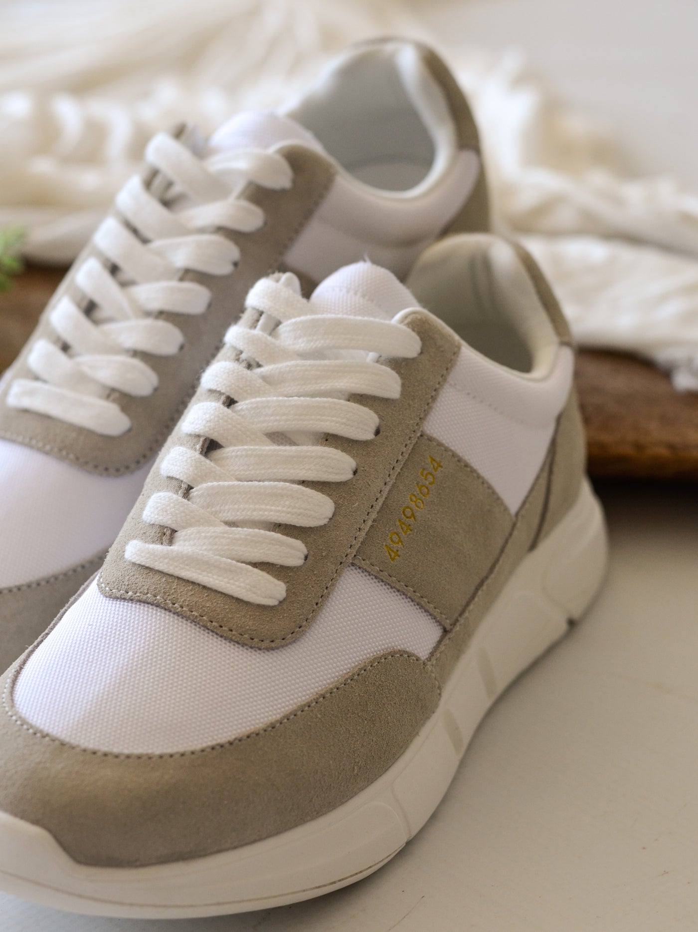 A tan and white chunky sneaker with white laces and gold number lettering decor on the middle outer upper of the shoe.