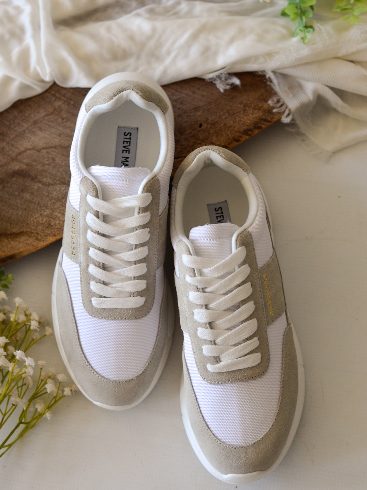 A tan and white chunky sneaker with white laces and gold number lettering decor on the middle outer upper of the shoe.