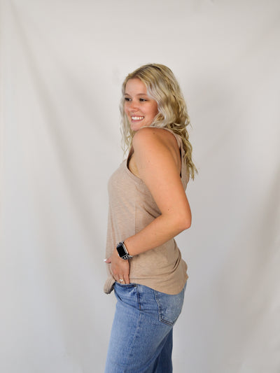 A model wearing a tan slub, relaxed fit tank top with a curved hem. Th model has it on with light wash denim jeans.