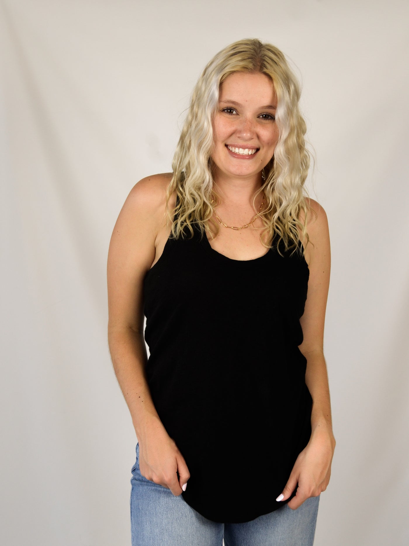 A model wearing a black slub, relaxed fit tank top with a curved hem. Th model has it on with light wash denim jeans.