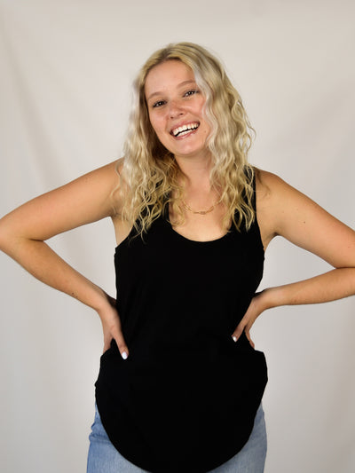 A model wearing a black slub, relaxed fit tank top with a curved hem. Th model has it on with light wash denim jeans.