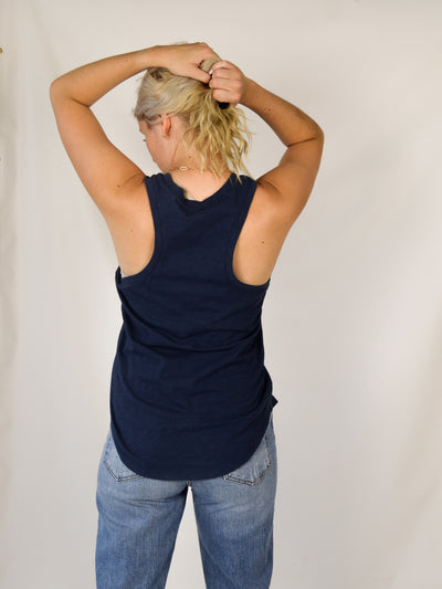 A model wearing a navy slub, relaxed fit tank top with a curved hem. Th model has it on with light wash denim jeans.